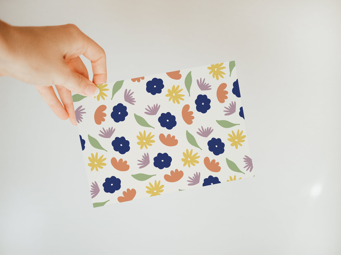hand holding an off-white greeting card with a colorful floral and leaf pattern in green, dark blue, orange, yellow, and lavender.
