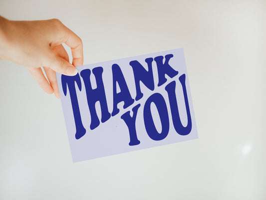 hand holding a light purple greeting card that says "Thank you" in darker purple font