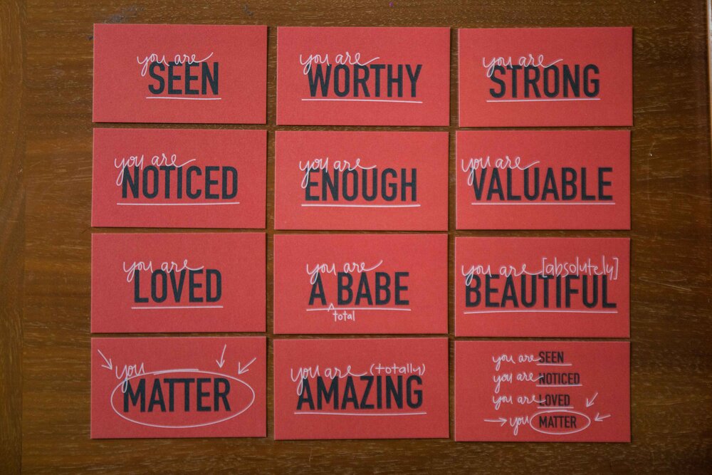 a set of 12 dark red mini cards with brown envelopes. Each card has one of twelve different sayings "you are seen", "you are worthy", "you are strong", "you are noticed", "you are enough", "you are valuable", "you are loved", "you are a total babe", "you are absolutely beautiful", "you matter", "you are totally amazing", and "you are seen, you are noticed, you are loved, you matter.". The back has a small "to" and "from" spot, with room to pen a short note.