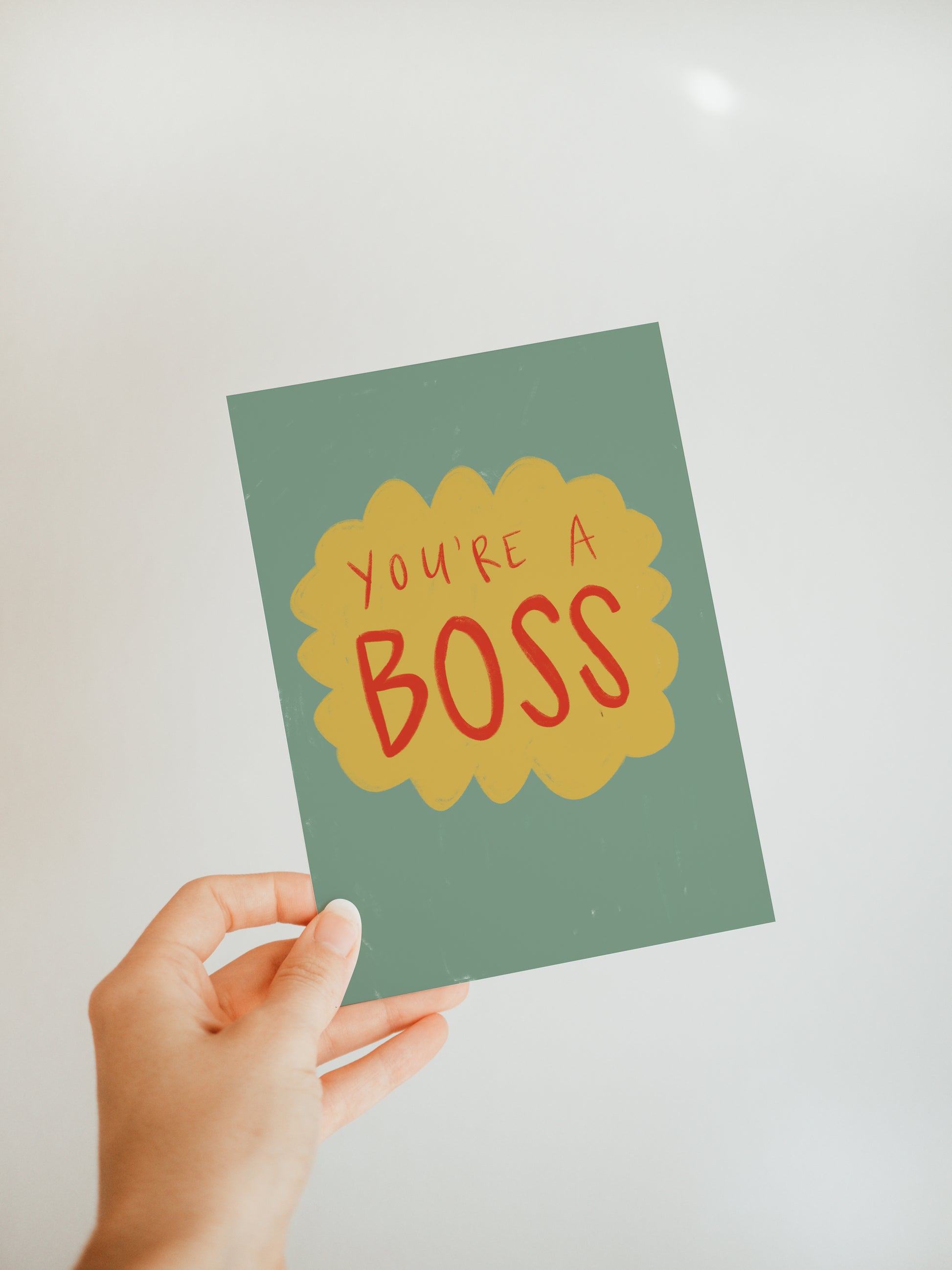 hand holding a green greeting card with a yellow bubble design with the words "you're a boss" inside in red font