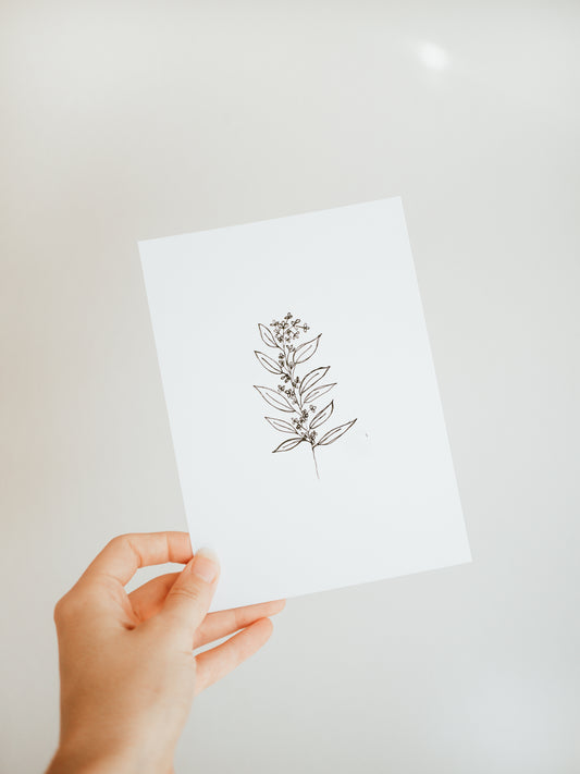 hand holding a white greeting card with a simple sketched design of a branch with leaves and berries in black.