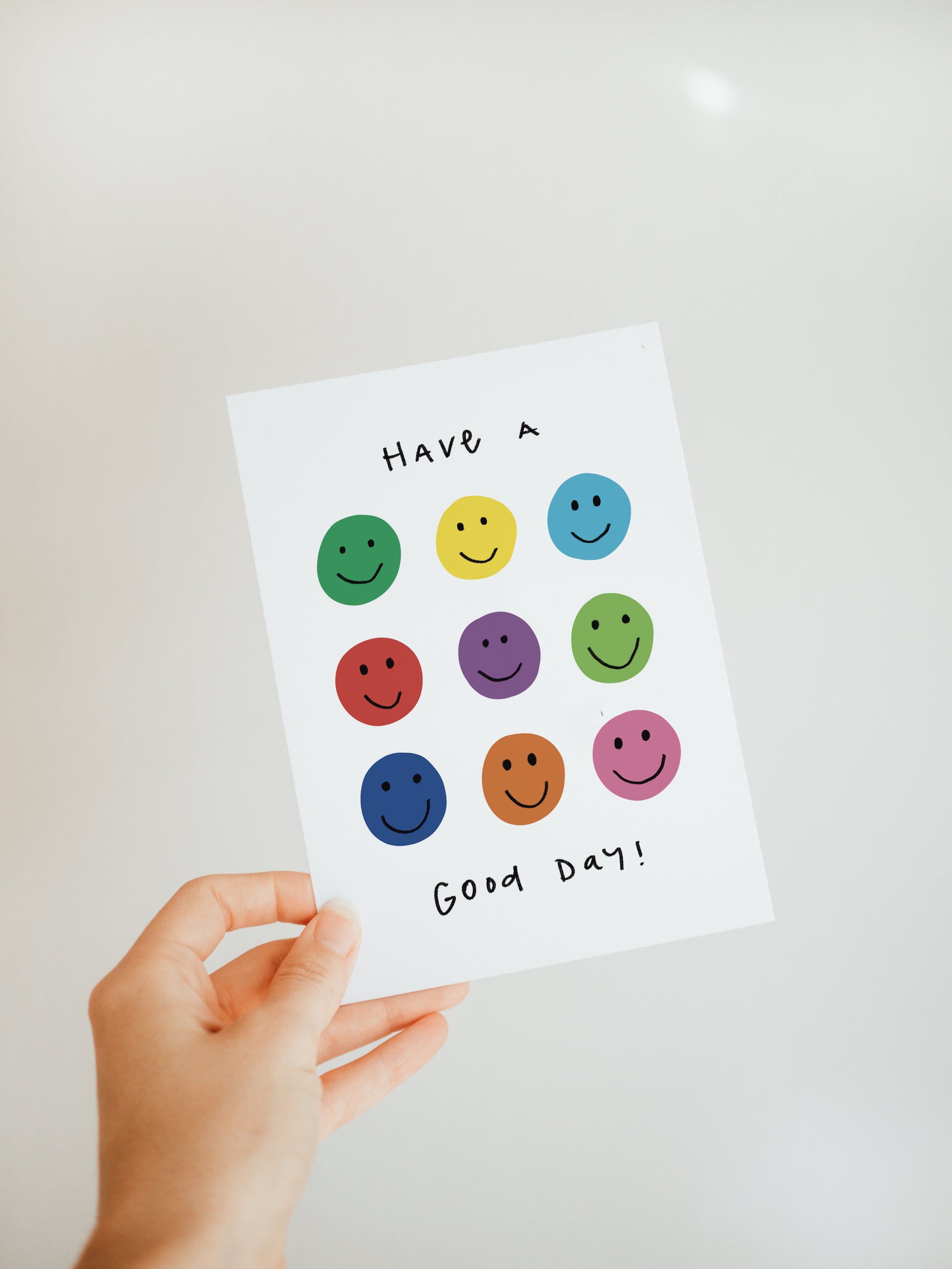 hand holding a white greeting card that has smiley faces in rainbow colors and says "Have a good day"