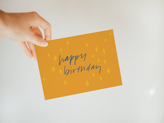 hand holding a golden yellow greeting card that says "happy birthday" with a small star design in the background