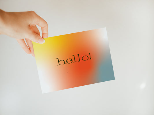 hand holding a multicolored greeting card that says "hello"