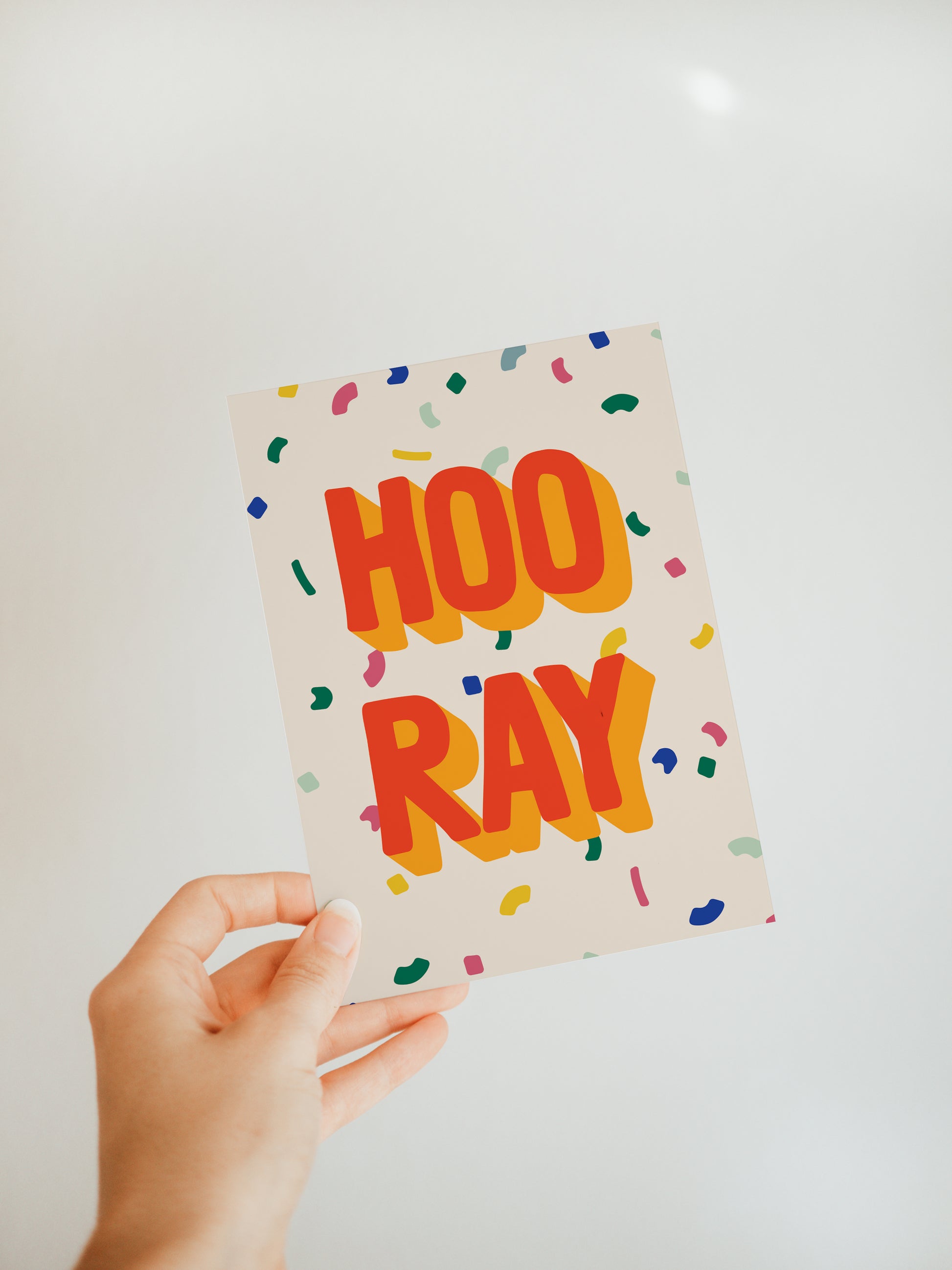 hand holding an off-white greeting card that says "hooray" with a colorful confetti background