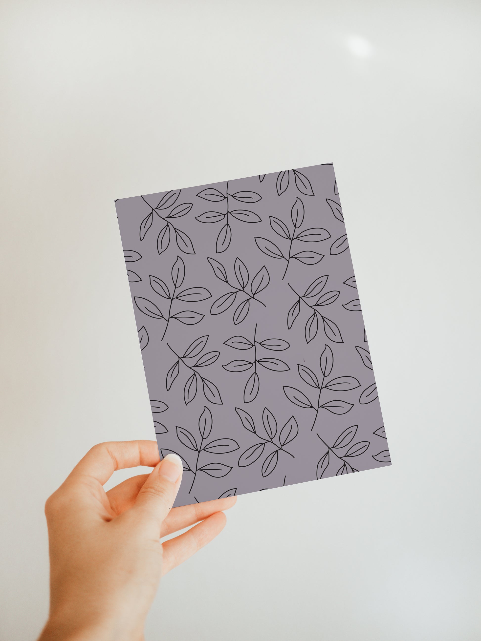 hand holding a dusky purple greeting card with a simple branch with leaves design repeated all over the front