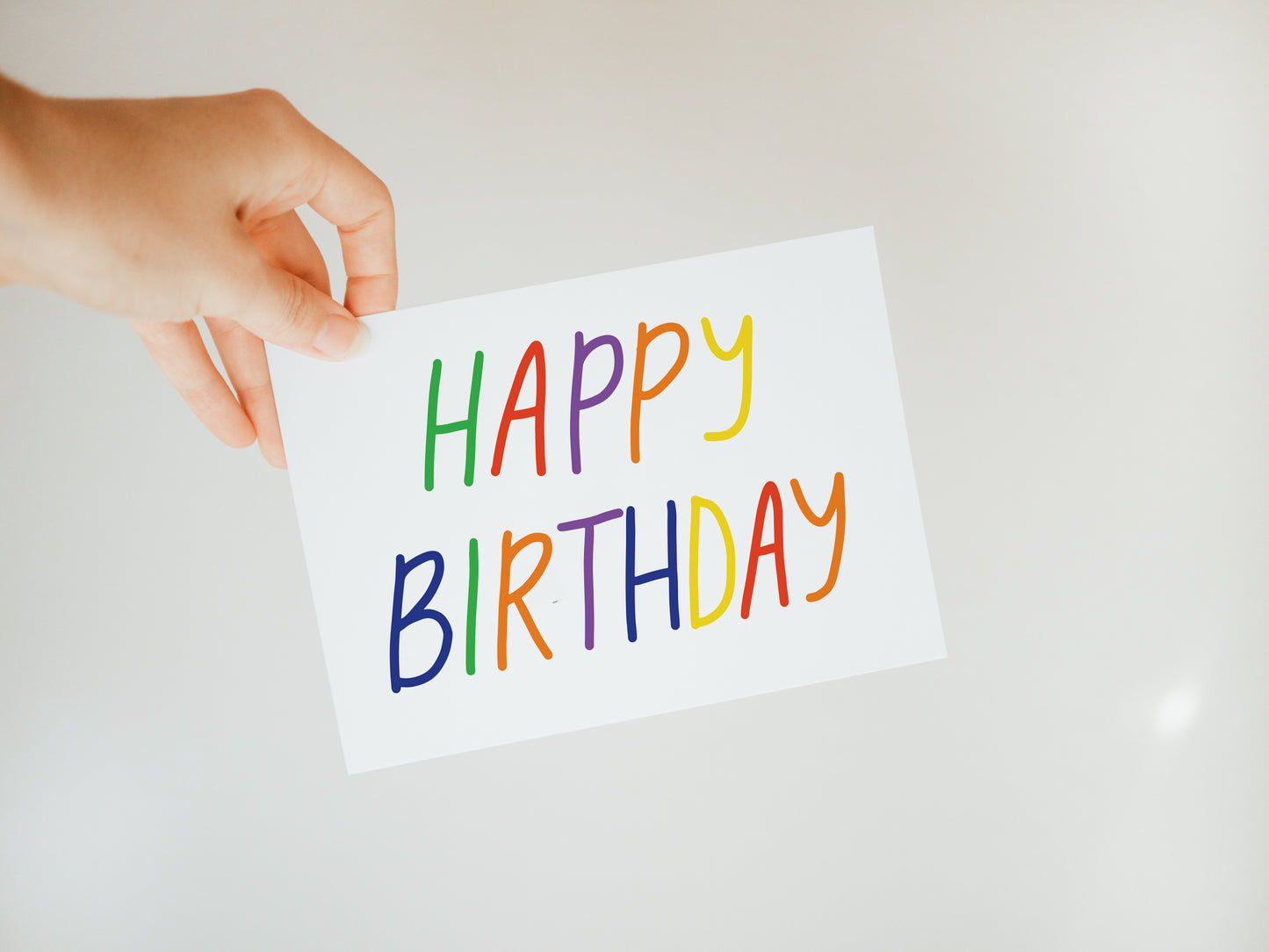 hand holding a white greeting card that says "happy birthday" in rainbow letters