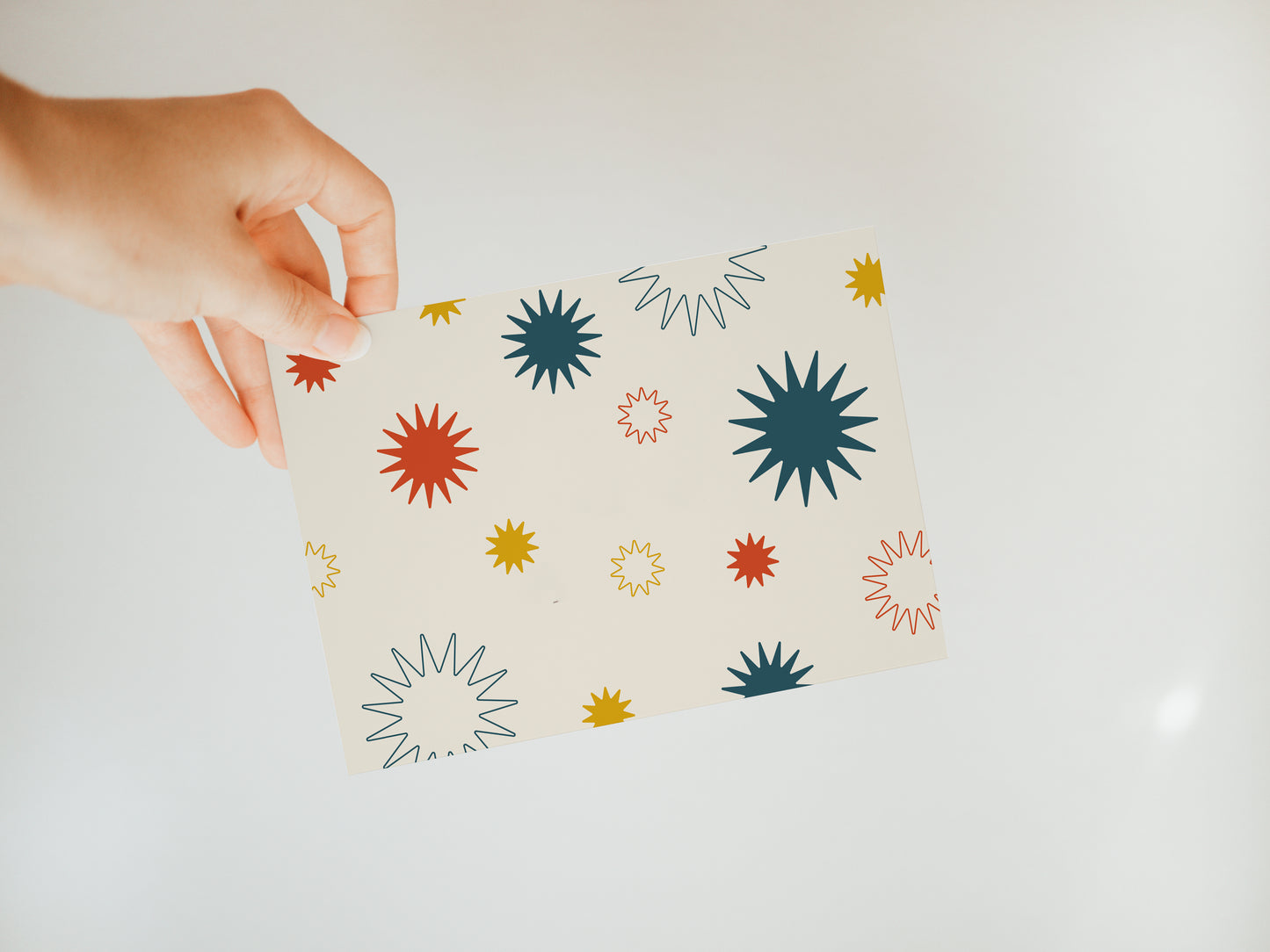 hand holding an off-white greeting card with red, blue, and gold sunburst designs