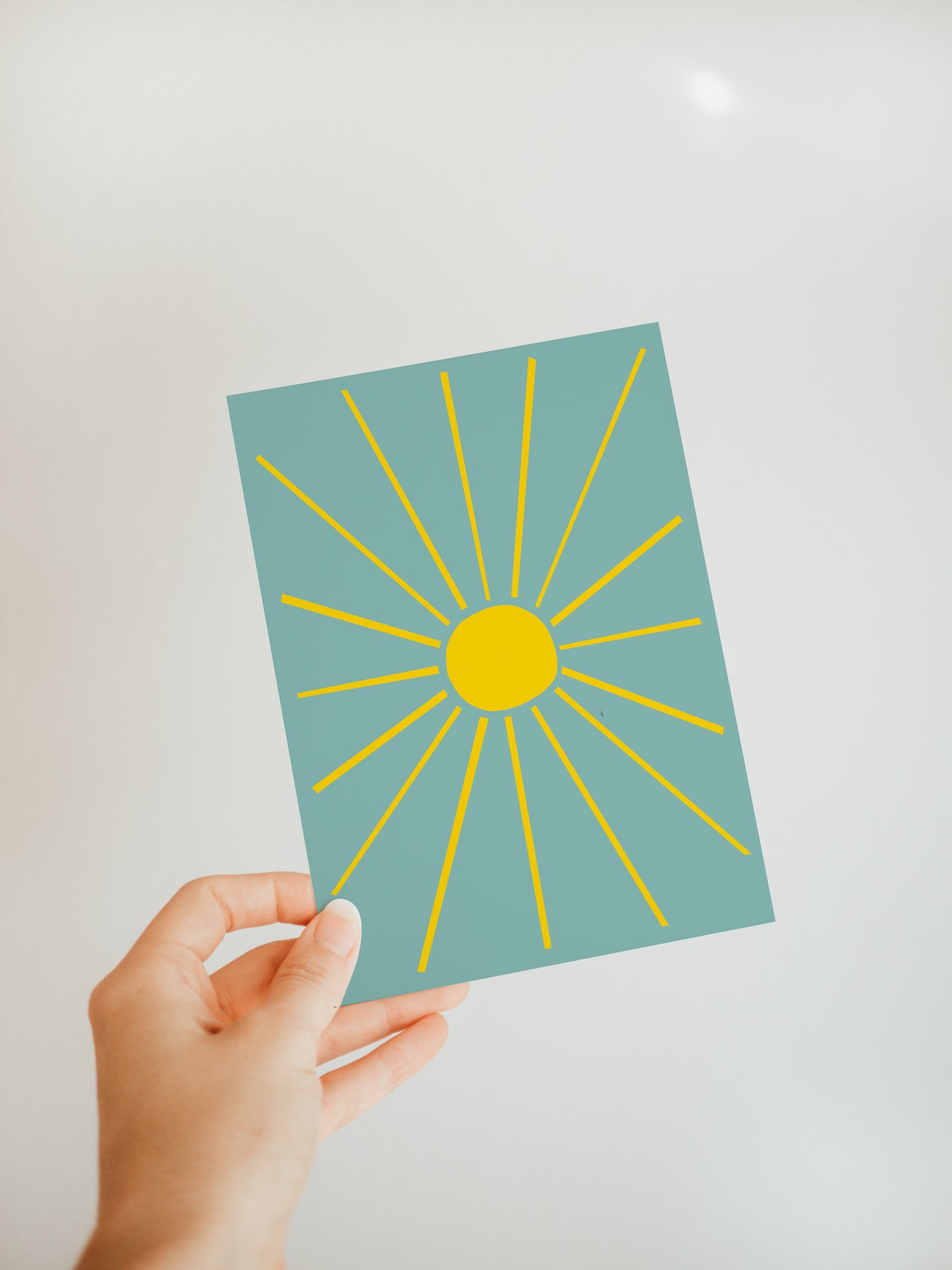 hand holding a blue greeting card with a bright yellow sun