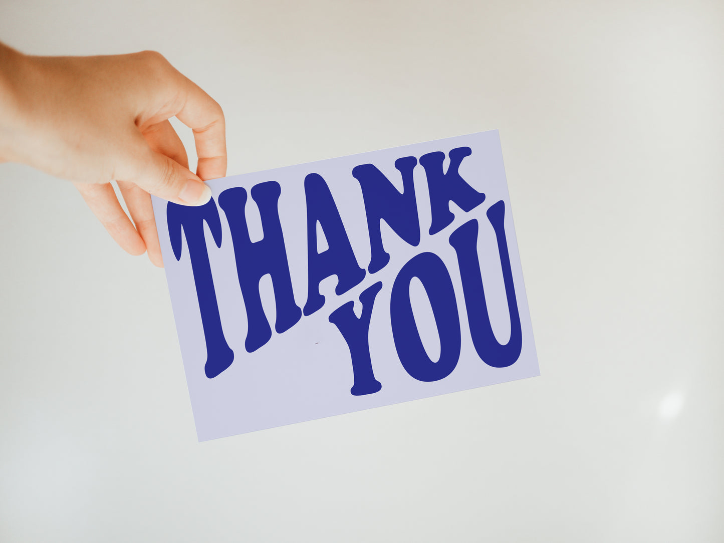 hand holding a light purple greeting card that says "Thank you" in darker purple font