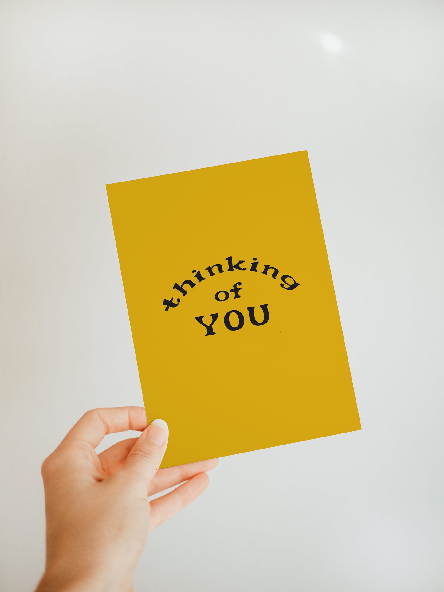 hand holding a golden yellow greeting card with the words "thinking of you" in black
