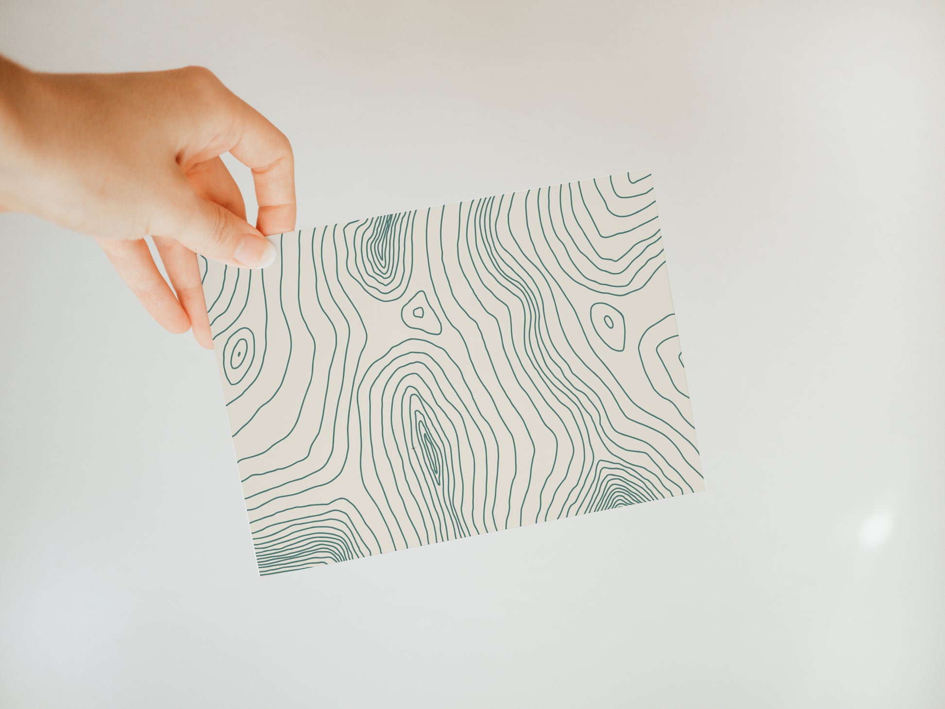 hand holding an off-white greeting card with a topography inspired line design in green covering the front