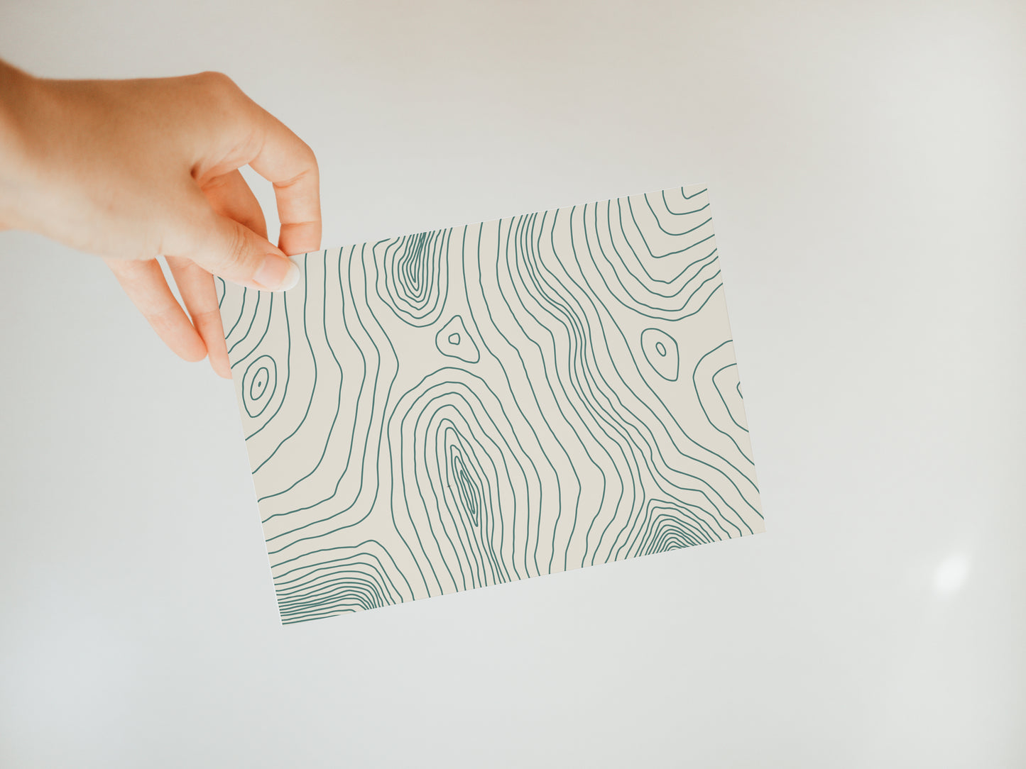 hand holding an off-white greeting card with a topography inspired line design in green covering the front