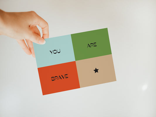hand holding a color block greeting card that says "you are brave" with blue, green, red, and brown background